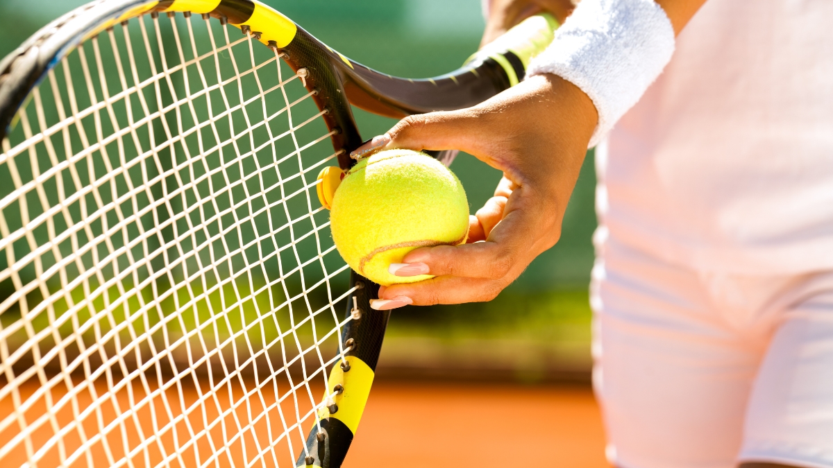 Close-up of a tennis player holding a ball and racket on a clay court during practice.