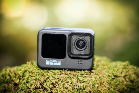 GoPro HERO12 Black action camera sitting on green moss in outdoor lighting.