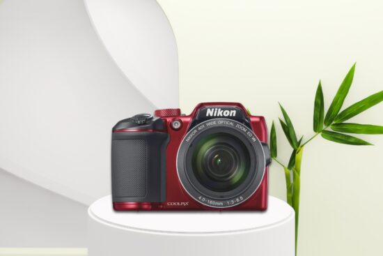 Red Nikon COOLPIX B500 camera with 40x optical zoom displayed on a white pedestal next to green leaves.