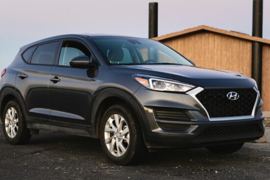 Dark gray Hyundai Tucson SUV parked near a wooden building by the water on a clear day.