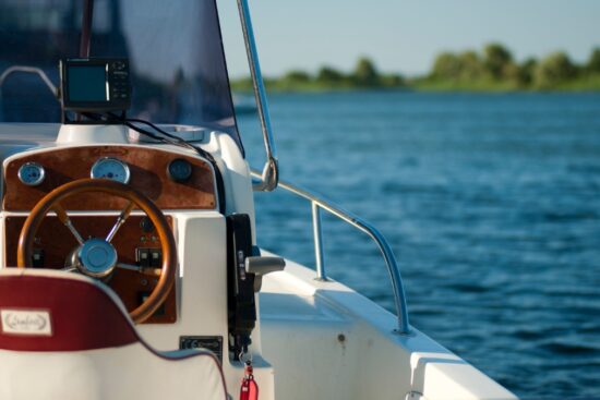 Boat steering console with wooden dash, gauges, and a Lowrance fish finder, set against a calm lake with clear blue skies and distant trees.