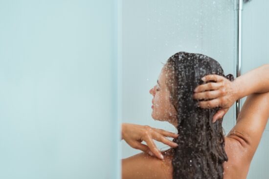 A woman takes a hot shower with steady water flow powered by a tankless water heater.