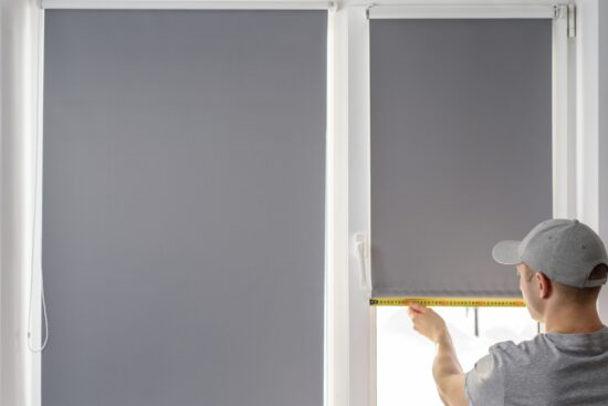 Man measuring a window while installing grey Persilux blackout blinds.