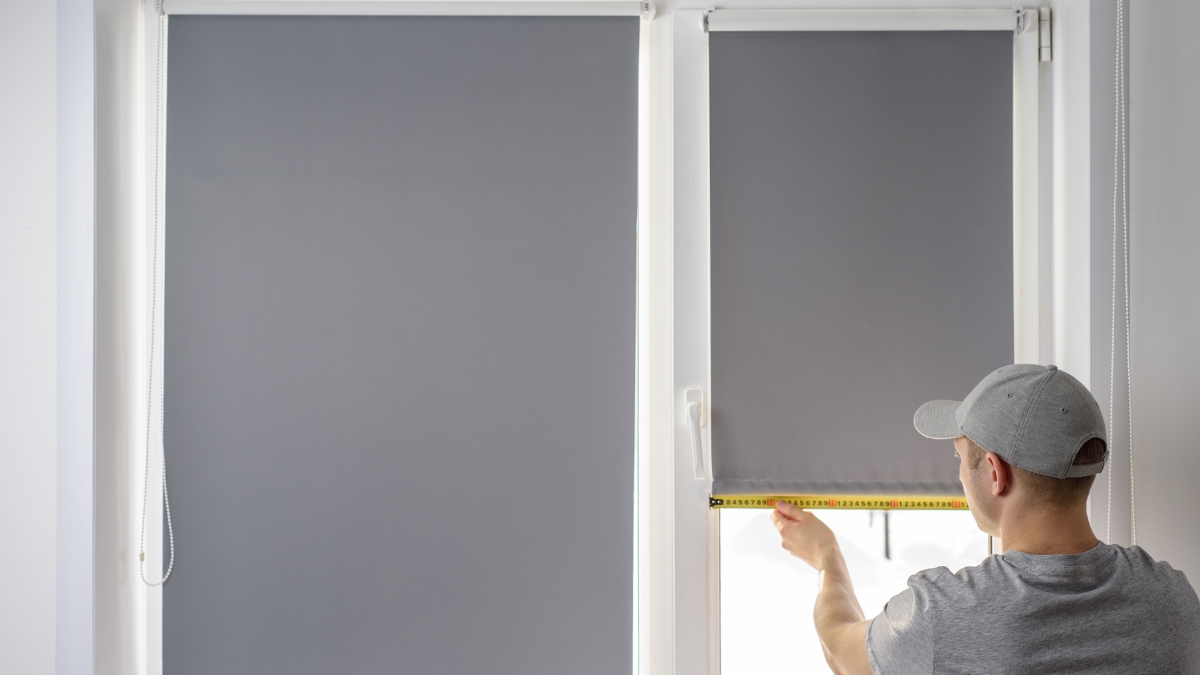 Man measuring a window while installing grey Persilux blackout blinds.