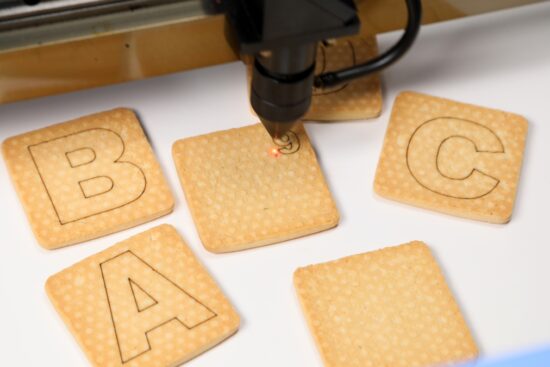 A laser engraver etching letters onto square cookies, showing precise detail and clean lines.