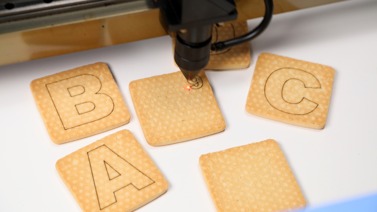 A laser engraver etching letters onto square cookies, showing precise detail and clean lines.