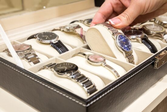 A person selecting a watch from a black leather watch case holding multiple wristwatches.