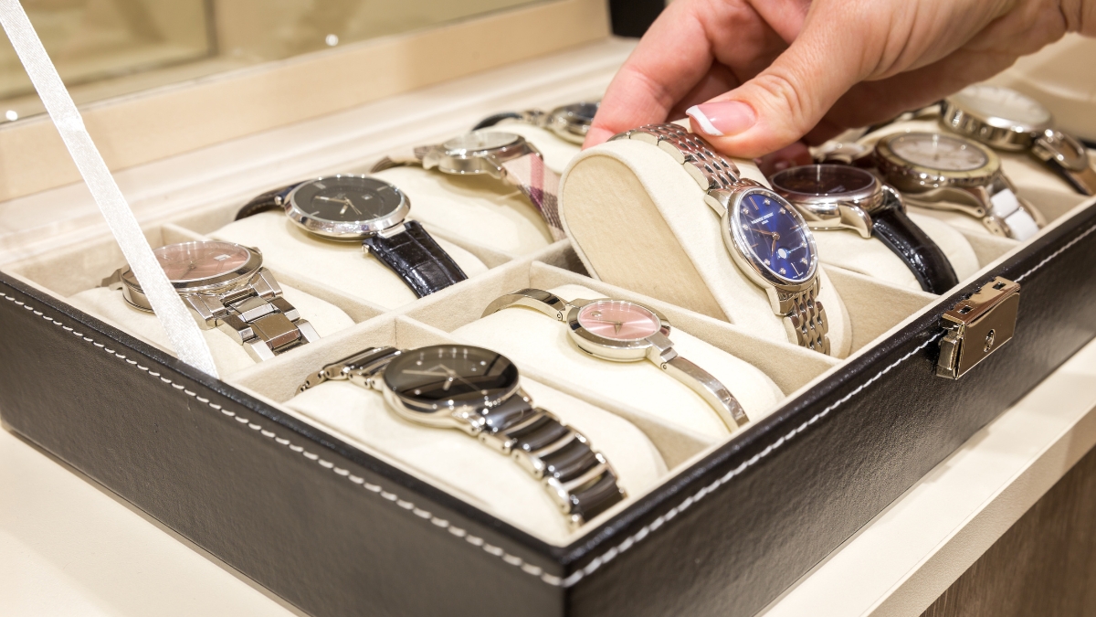 A person selecting a watch from a black leather watch case holding multiple wristwatches.