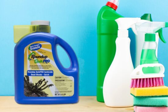 Roundup QuickPro dry formula herbicide jug placed beside cleaning bottles and sponges on a wooden surface.