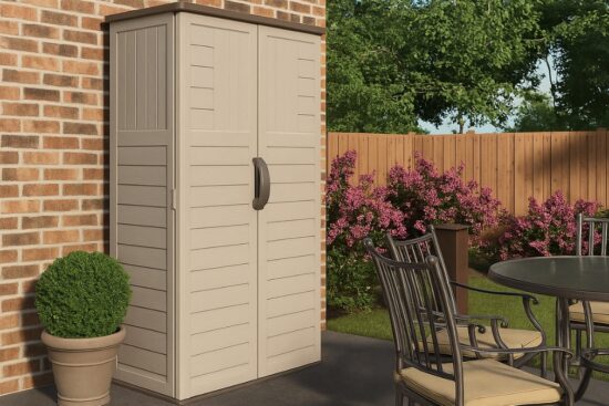 Suncast vertical outdoor storage shed placed on a patio next to a brick wall and garden seating area.