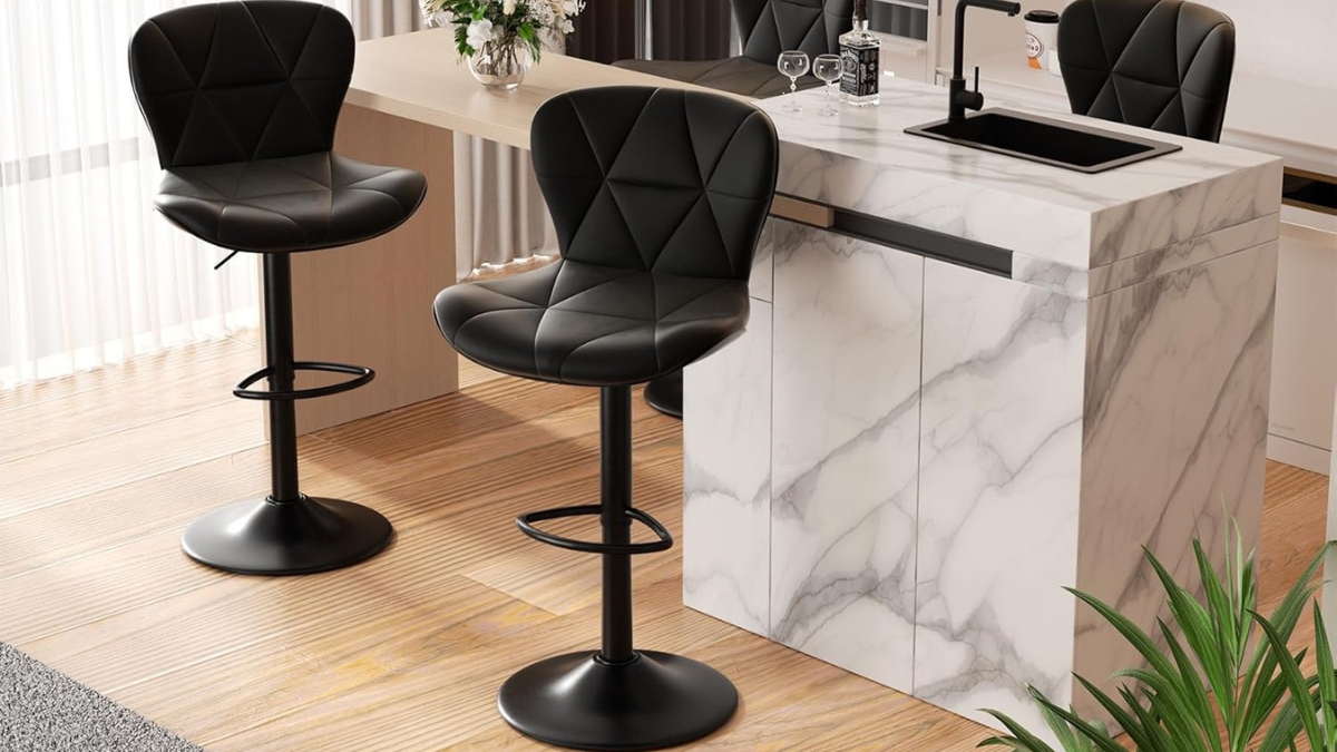 Two modern black bar stools with backs placed by a marble kitchen island in a bright room.