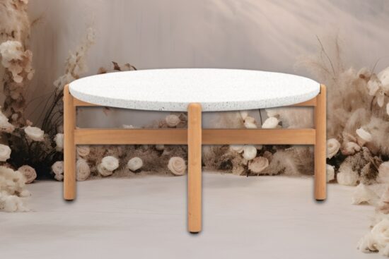 Round terrazzo top coffee table with a natural wood base placed in front of soft floral decor.