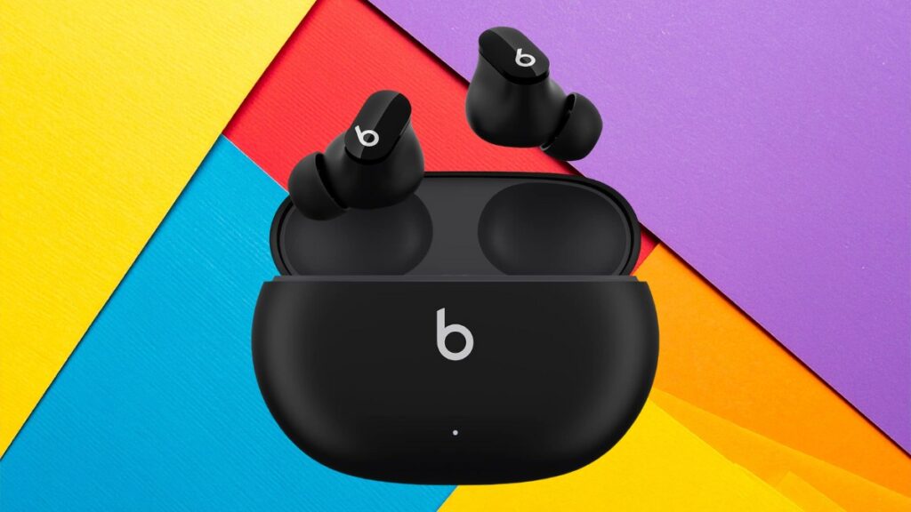 Black Beats Studio Buds wireless earbuds with charging case displayed on a colorful geometric background of yellow, blue, red, and purple panels.