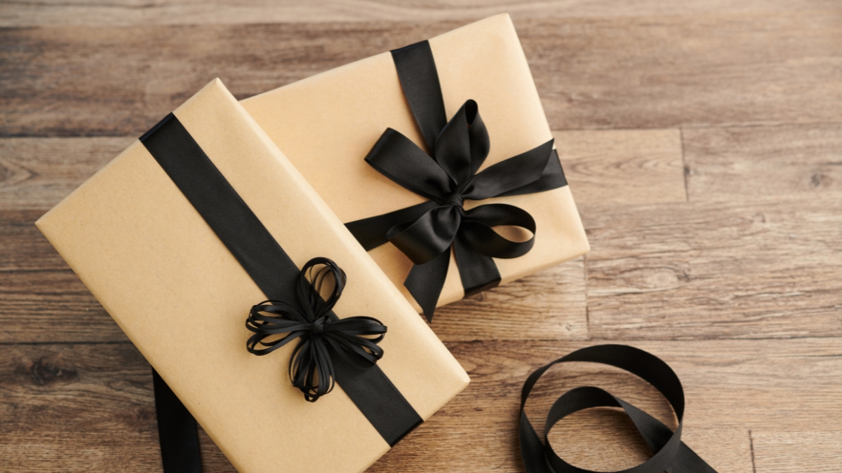 Two brown gift boxes wrapped with black ribbon bows on a wooden surface.