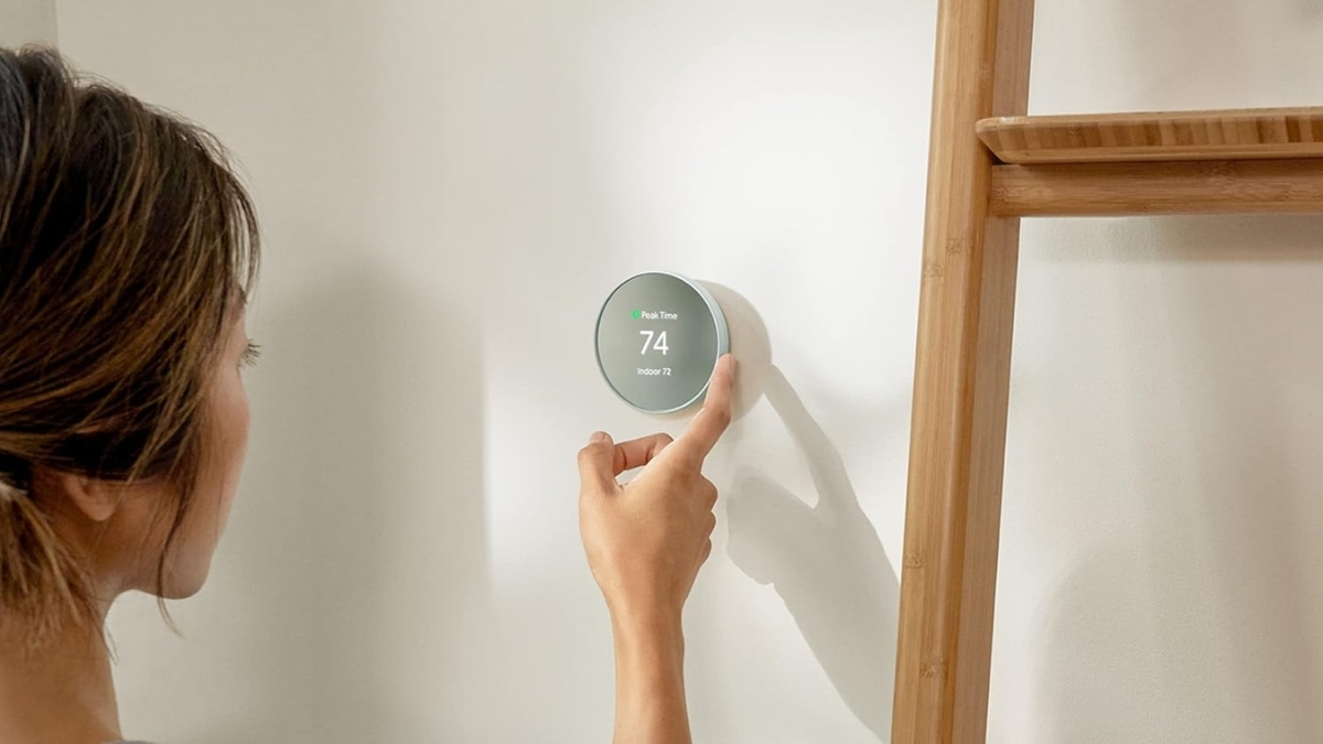 Person adjusting a Google Nest Thermostat on a wall, showing 74 degrees on the display for smart home temperature control.