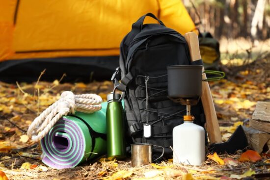 Essential camping gear setup featuring a tent, backpack, sleeping bag, and outdoor cooking supplies at a campsite.